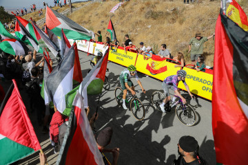 Varios ciclistas pasan por una zona con protestas propalestinas durante la 20ª etapa de la Vuelta Ciclista a España