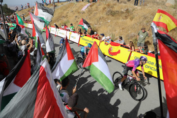 Varios ciclistas pasan por una zona con protestas propalestinas durante la 20ª etapa de la Vuelta Ciclista a España.