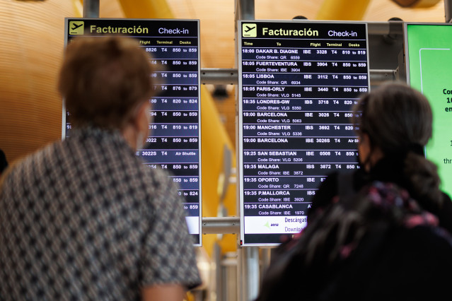 Archivo - Dos personas miran el panel de facturación de la Terminal 4 (T4) del aeropuerto Adolfo Suárez Madrid-Barajas