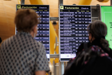Archivo - Dos personas miran el panel de facturación de la Terminal 4 (T4) del aeropuerto Adolfo Suárez Madrid-Barajas