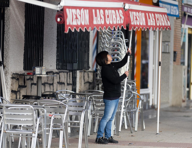 Archivo - Una camarera levanta el toldo de un bar, en Madrid (España).