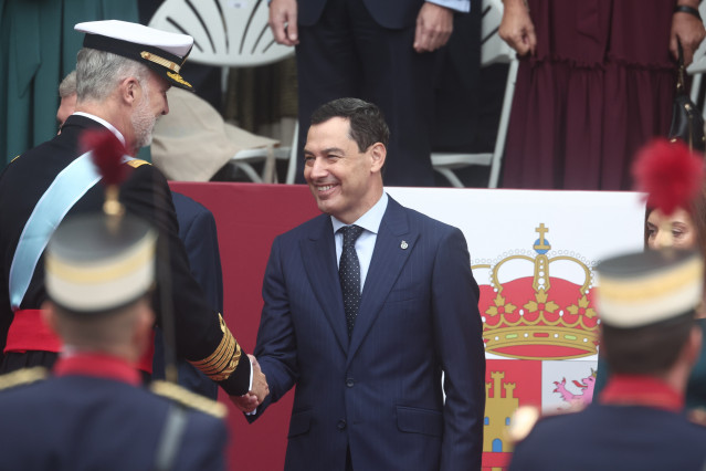El rey Felipe y el presidente de la Junta de Andalucía, Juanma Moreno,  durante el acto solemne de homenaje a la bandera nacional y desfile militar por el 12 de octubre, Día de la Hispanidad, en la Plaza de Cánovas del Castillo, a 12 de octubre de 2025, e