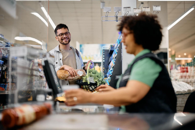 Archivo - Hombre pasando por la caja de un supermercado.