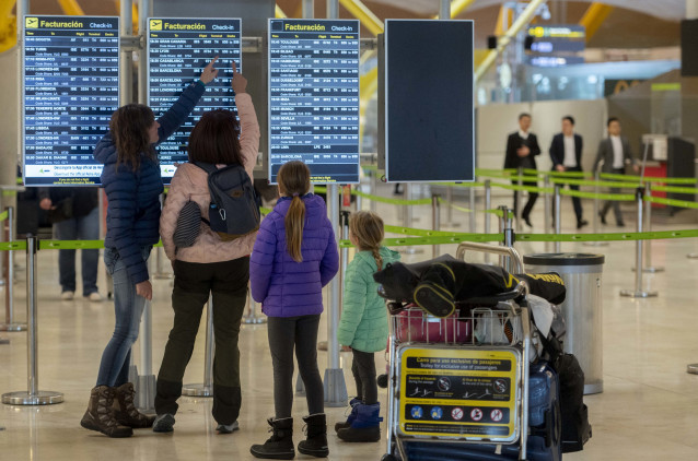 Archivo - Varias personas observan las salidas de los vuelos.