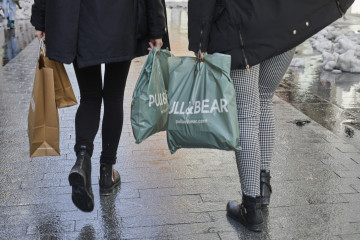 Archivo - Dos personas caminan con bolsas.