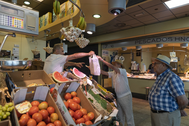 Archivo - Un trabajador autónomo entrega su compra a un cliente en un mercado de abastos