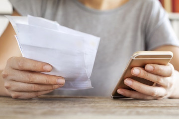 Archivo - Persona sujeta un teléfono y una factura