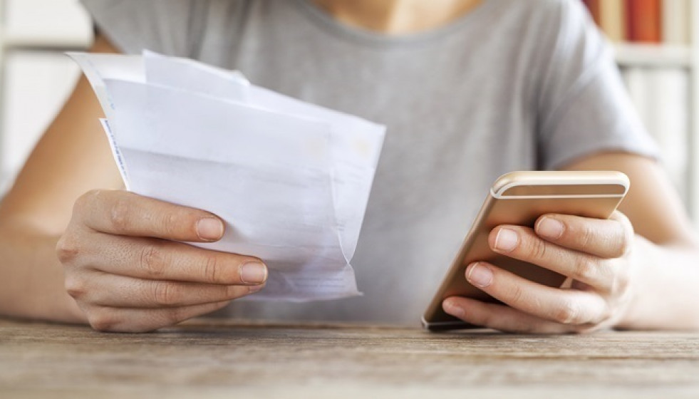Archivo - Persona sujeta un teléfono y una factura