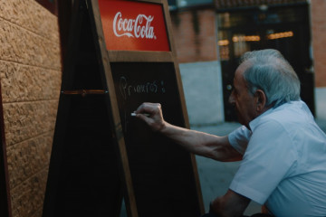 Camarero escribiendo menú en pizarra de Coca-Cola.