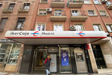 Archivo - Una mujer entra en un una oficina de IberCaja en Madrid.