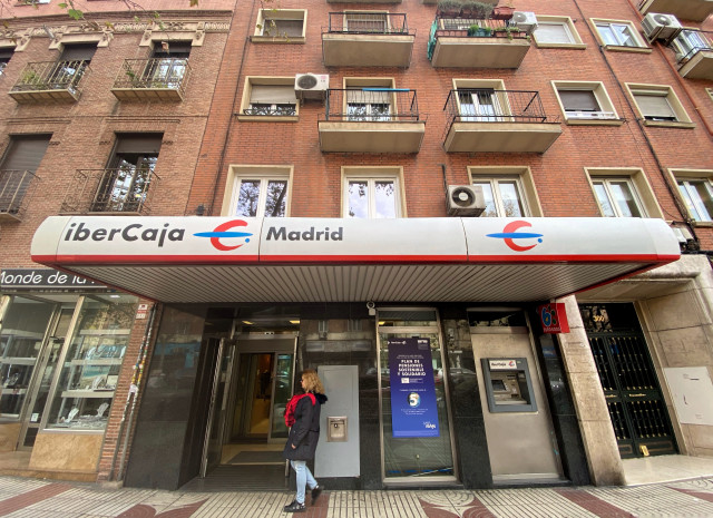 Archivo - Una mujer entra en un una oficina de IberCaja en Madrid.