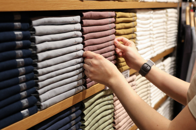 Archivo - Una dependienta coloca la ropa en una tienda de moda