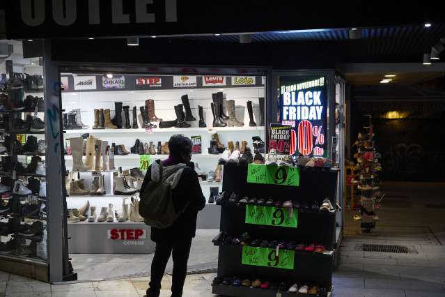 Archivo - Personas delante de un comercio anunciando descuentos por el Black Friday