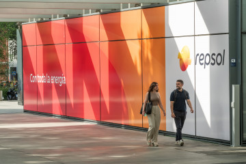 Archivo - Empleados pasando por delante del panel de entrada a Campus con el nuevo logo de Repsol