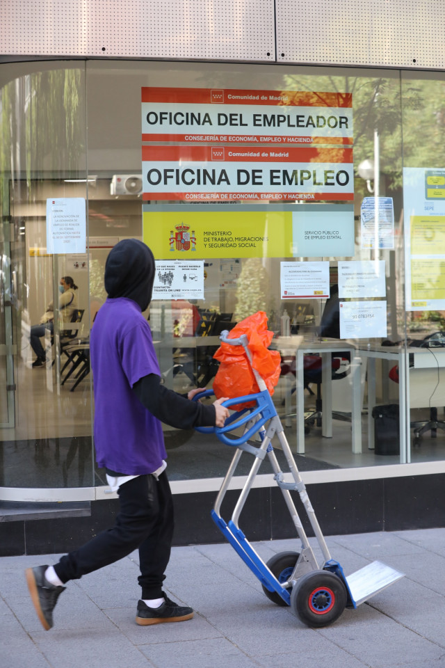 Archivo - Un joven pasa con una carretilla por una oficina de empleo de Madrid