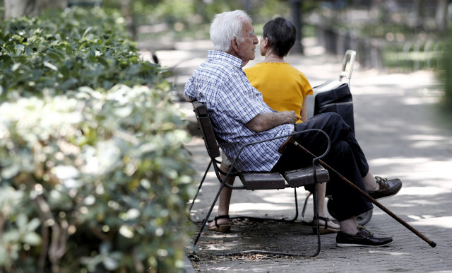 Archivo - Un pensionista descansa en un banco de un parque de Madrid, junto a una mujer más joven