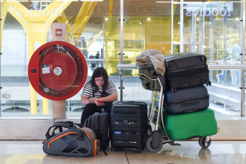 Archivo - Una viajera espera el embarque junto a su equipaje en una terminal de aeropuerto.