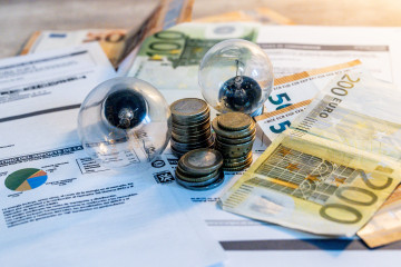 Archivo - Dos bombillas sobre billetes, monedas y facturas