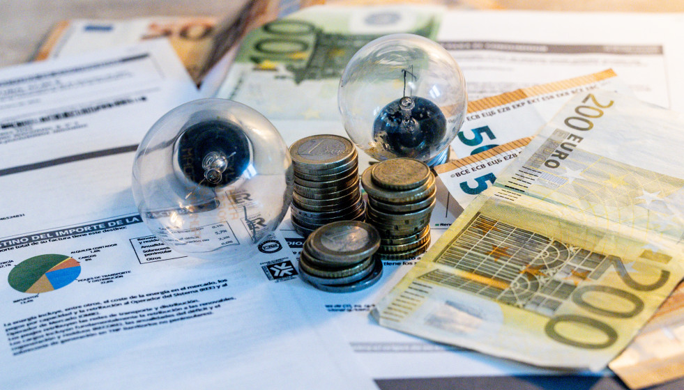 Archivo - Dos bombillas sobre billetes, monedas y facturas