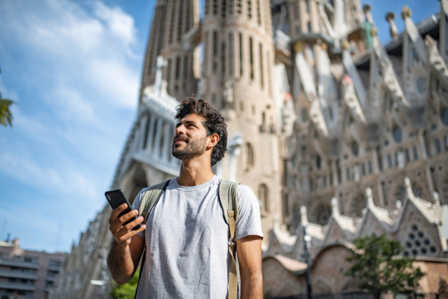Archivo - Vista de un  turista hispano de 30 años usando un teléfono inteligente como guía turística, con la Sagrada Familia de fondo