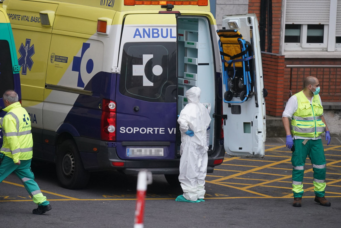 Varios sanitarios protegidos, uno con un traje y otro con mascarilla y guantes de látex, junto a una ambulancia en el Hospital Universitario Cruces, uno de los hospitales públicos vascos de referencia para infectados por coronavirus, en Bilbao/Euskadi (Es