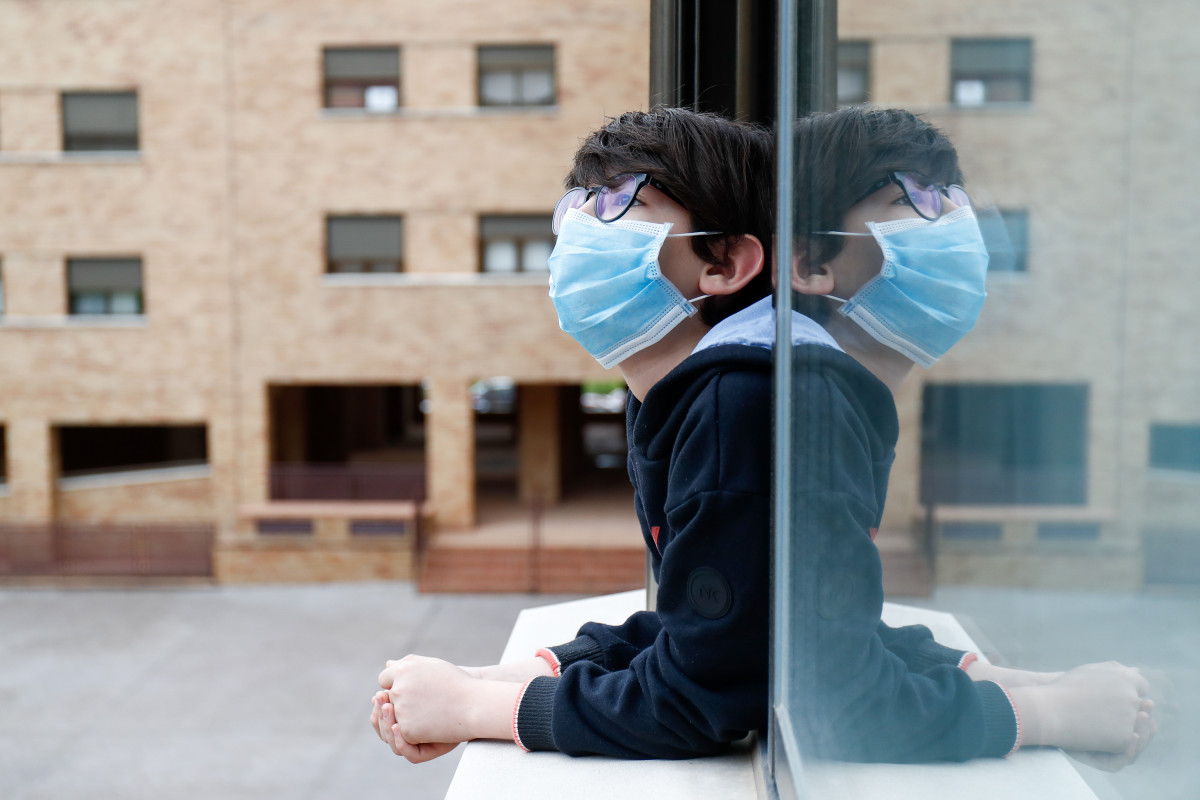 Un niño con una mascarilla se asoma a la ventana de su casa durante el confinamiento por el coronavirus, en Valdemoro/Madrid (España) a 20 de abril de 2020.