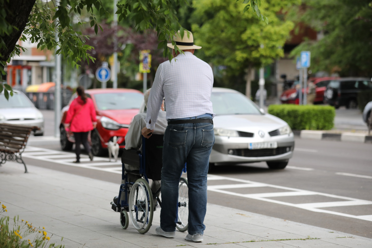 Un hombre pasea a una persona de edad avanzada en silla de ruedas durante su franja horaria permitida en la desescalada por la crisis del Covid-19 donde aquellos mayores de 70 años pueden salir a la vía pública de 10.00 a 12.00 horas y de 19.00 a 20.00 ho