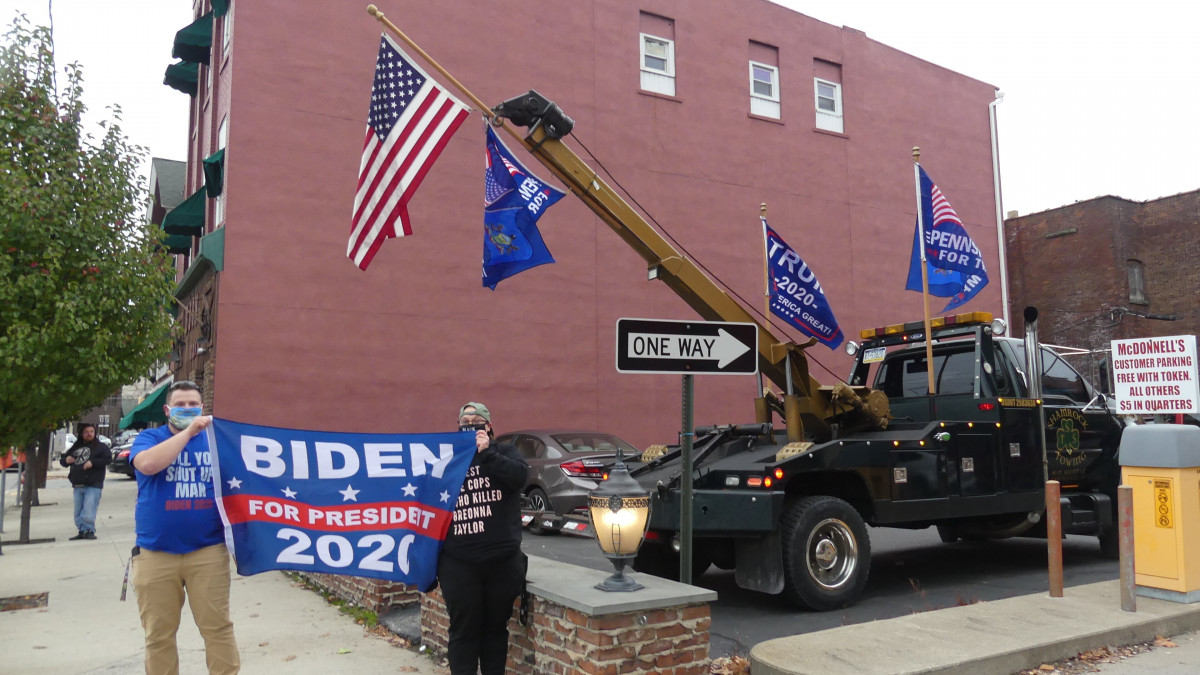 Partidarios de Joe Biden muesta un cartel a super favor junto a banderas a favor de Donald Trump en Pensilvania