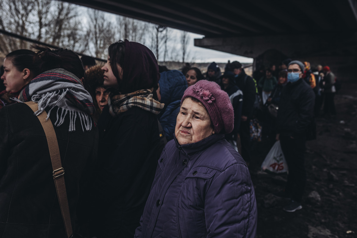 Una dona gran al costat de més persones espera per travessar el riu d'Irpín.