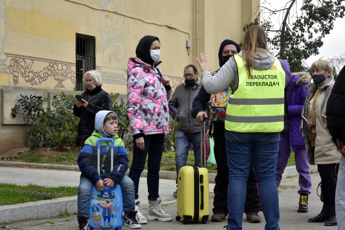 Varias personas refugiadas hablan con una traductora frente al palacio de Victoria Eugenia, el palacio 7 de Fira de Barcelona, convertido en un centro de recepción y atención de refugiados de Ucrani